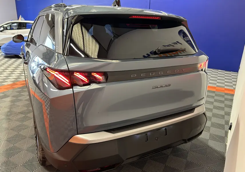 Vue 3/4 arrière droite du Peugeot 5008 bleu Ingaro avec feux arrière LED allumés et hayon fermé en intérieur showroom.
