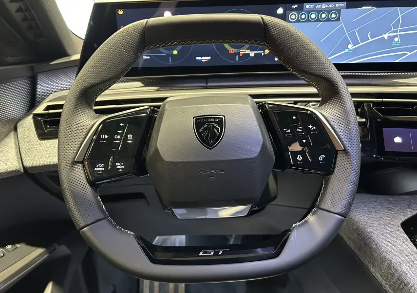 Vue rapprochée du volant cuir perforé noir avec logo Peugeot et inscription GT du Peugeot 5008 III Hybrid 2026.
