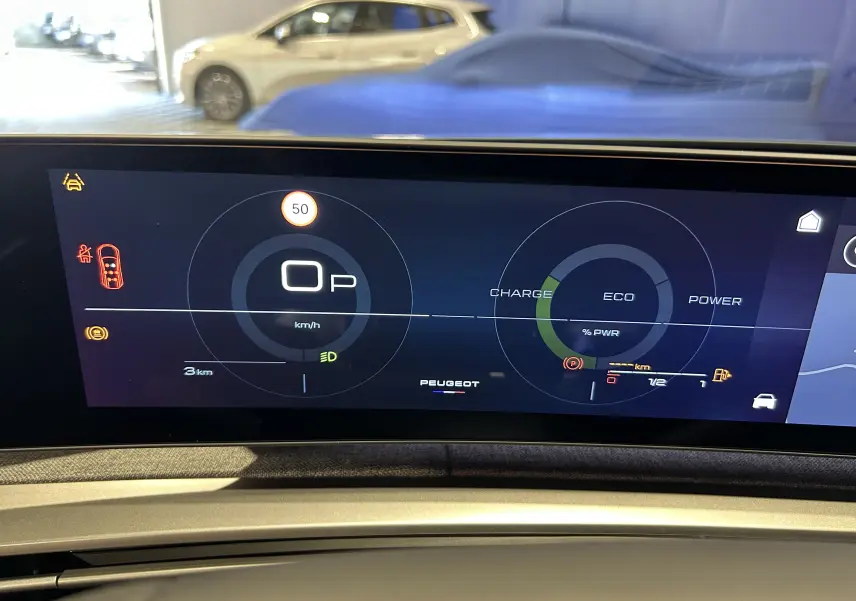 Écran numérique du tableau de bord du Peugeot 5008 III Hybrid 145 GT, affichant la vitesse et la charge hybride, vue intérieure.