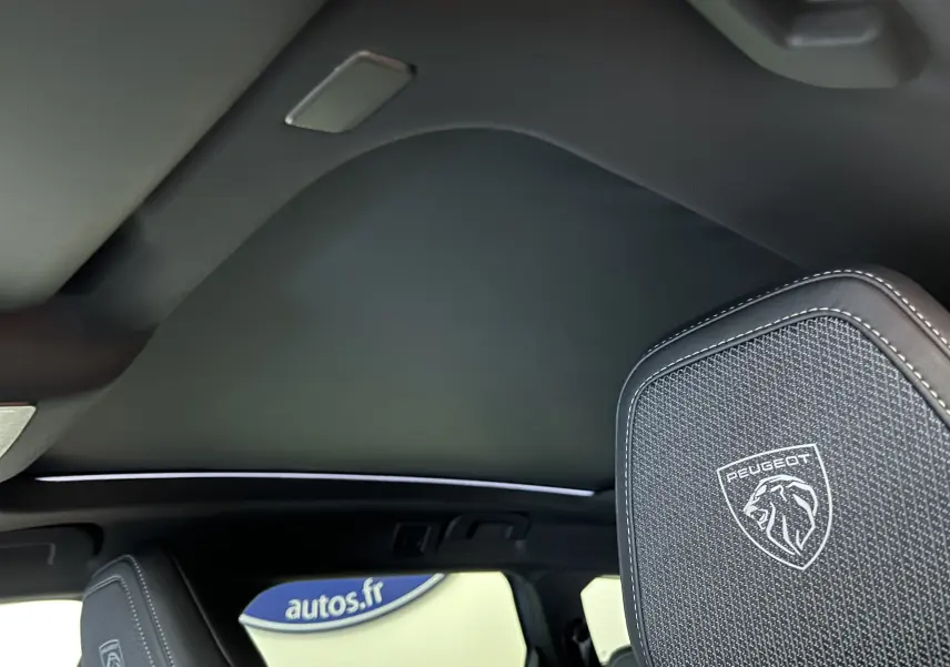 Vue intérieure du toit ouvrant panoramique et appuie-tête avant avec logo Peugeot sur un 5008 bleu Ingaro.