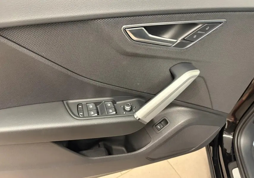Gros plan sur la porte avant gauche de l’Audi Q2 Noir Mythic, montrant les commandes des vitres et la poignée intérieure argentée.