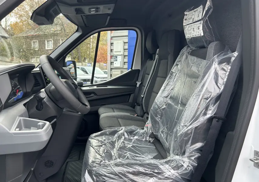 Vue intérieure côté conducteur du Renault Master blanc 2025, sièges avant en tissu protégés par film plastique.