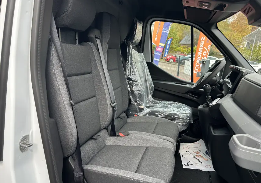Vue intérieure côté conducteur du Renault Master blanc 2025, montrant les sièges avant en tissu gris et le volant.