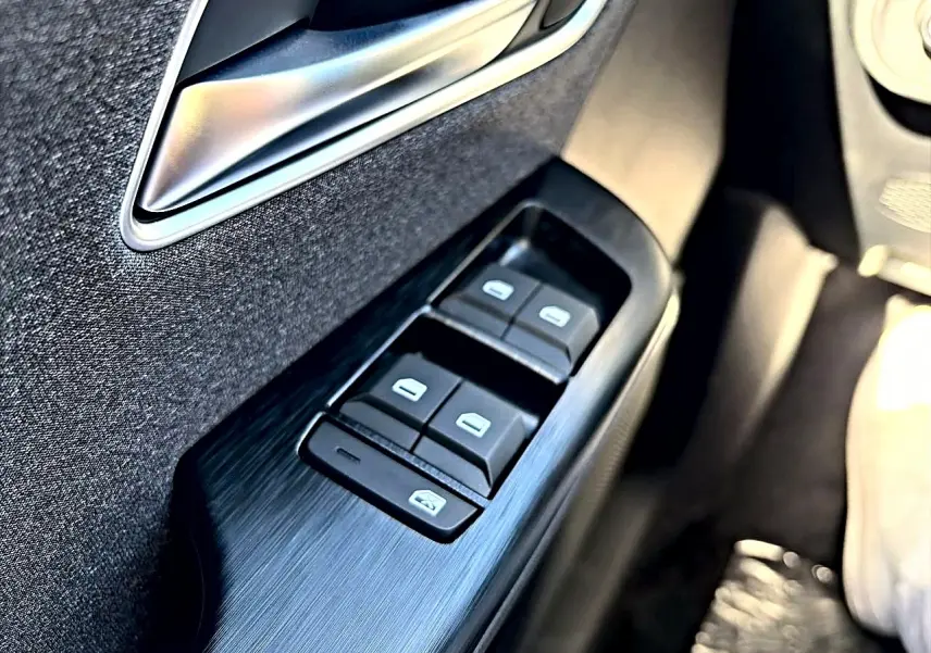 Gros plan sur les commandes des vitres électriques côté conducteur d’un MG Motor ZS noir hybride 2026.