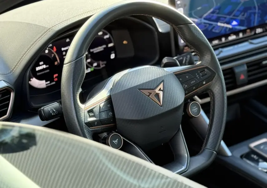 Gros plan sur le volant en cuir perforé avec logo CUPRA et tableau de bord numérique du Leon ST noir Midnight.
