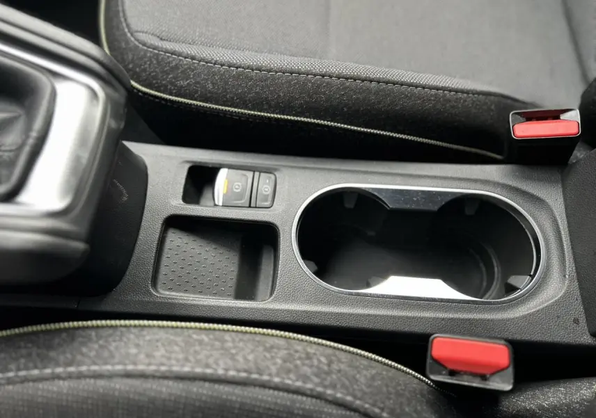 Gros plan sur la console centrale noire du Renault Captur 2025, avec porte-gobelets et bouton frein à main électrique.