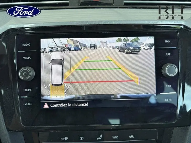 Écran de caméra de recul montrant l'arrière d'une Volkswagen Passat SW gris manganèse avec repères de distance colorés.