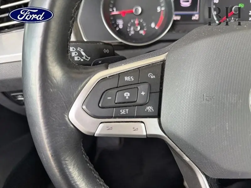 Gros plan sur les commandes au volant cuir noir d'une Volkswagen Passat SW, avec tableau de bord flou en arrière-plan.