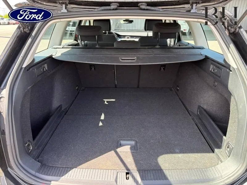 Coffre ouvert vu de l'arrière d'une Volkswagen Passat SW gris manganèse métallisé, espace de chargement spacieux et tapis noir.