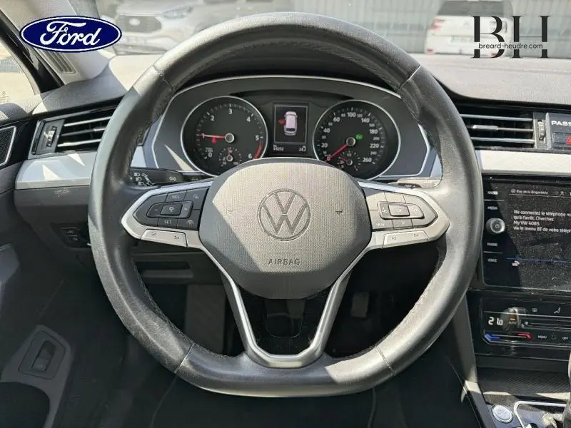 Vue intérieure centrée sur le volant cuir Volkswagen d'une Passat SW 2.0 TDI, avec tableau de bord et écran tactile visibles.