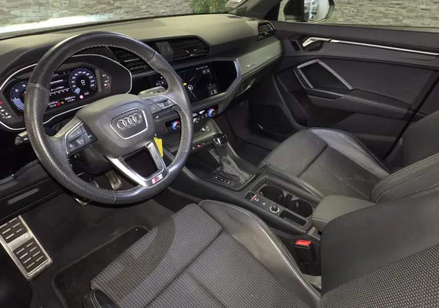 Vue intérieure côté conducteur de l'Audi Q3 Sportback 2023 noire, volant cuir S line et tableau de bord numérique.