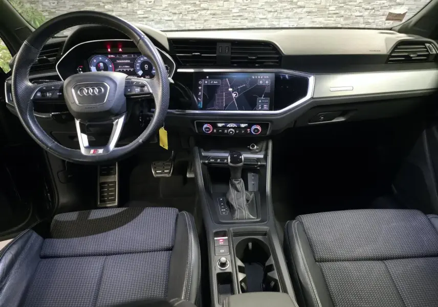 Vue intérieure avant de l'Audi Q3 Sportback noir, tableau de bord moderne avec écran tactile et volant multifonctions cuir.