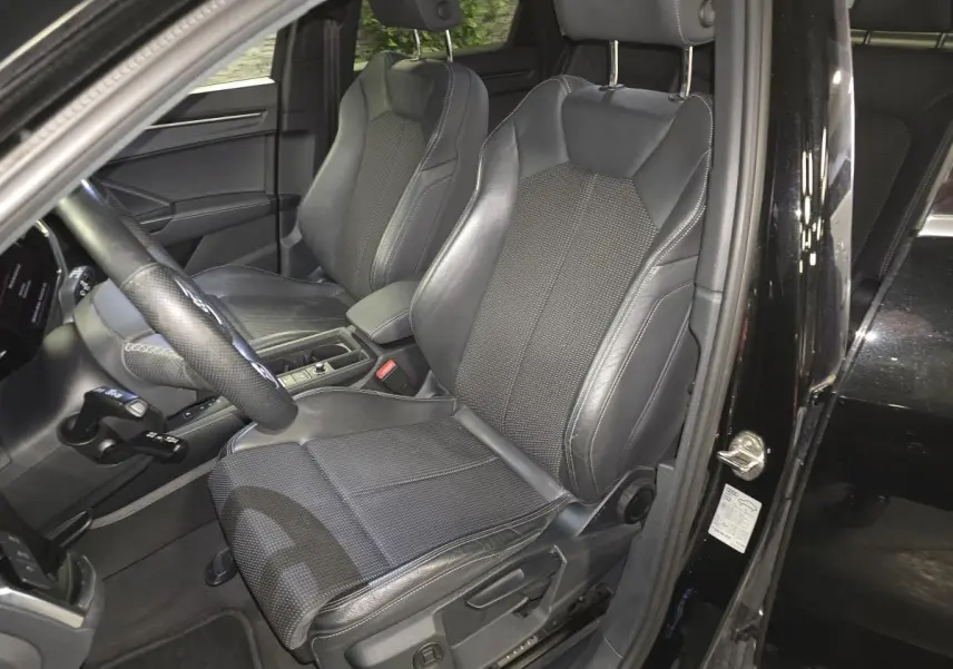 Vue intérieure côté conducteur de l'Audi Q3 Sportback noir 2023, sièges sport en cuir et tissu avec surpiqûres grises.