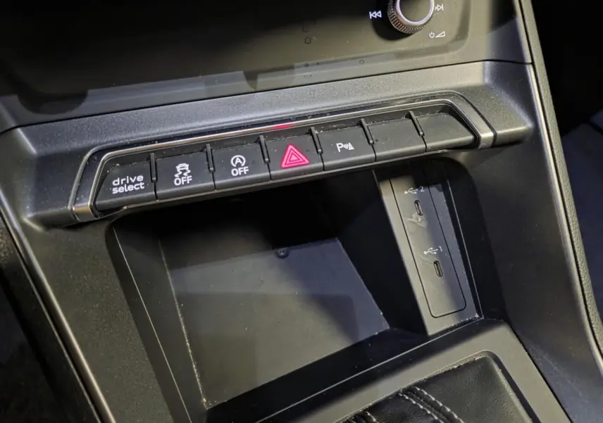 Gros plan sur la console centrale noire de l'Audi Q3 Sportback 2023 avec boutons de contrôle et deux ports USB-C visibles.