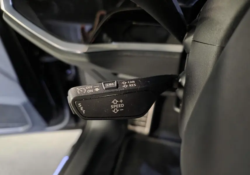 Gros plan sur la commande de régulateur de vitesse noire à gauche du volant dans l’Audi Q3 Sportback noir 2023.