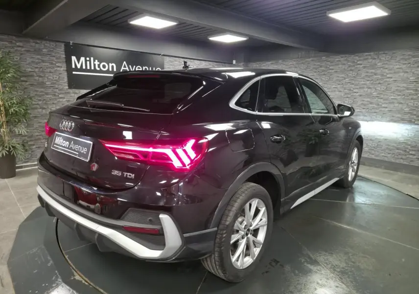 Audi Q3 Sportback noir vue 3/4 arrière droit, feux LED allumés et jantes aluminium 5 branches visibles.