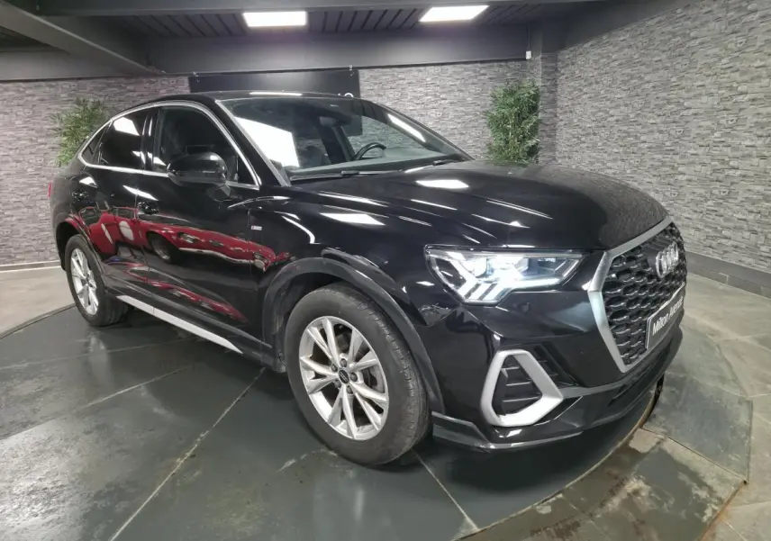 Audi Q3 Sportback noir vue 3/4 avant droit en intérieur, avec calandre hexagonale et jantes 5 branches.