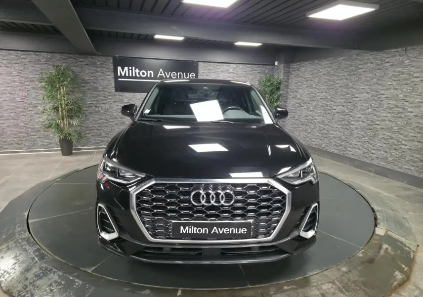 Audi Q3 Sportback noir vue de face en intérieur, calandre hexagonale et phares LED distinctifs visibles.