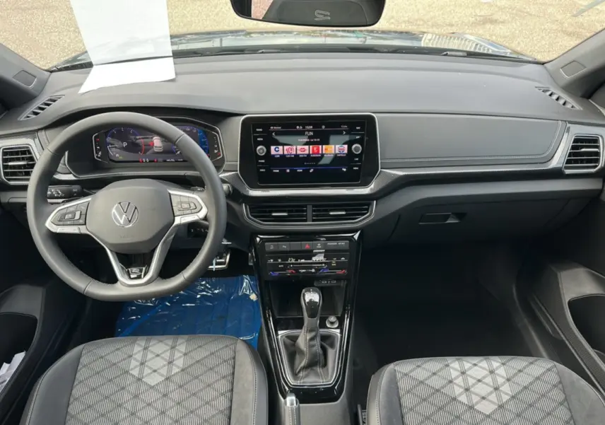Vue intérieure avant du Volkswagen T-Cross TSI 116 DSG7 R-Line 2025 avec tableau de bord numérique et sièges tissu gris.
