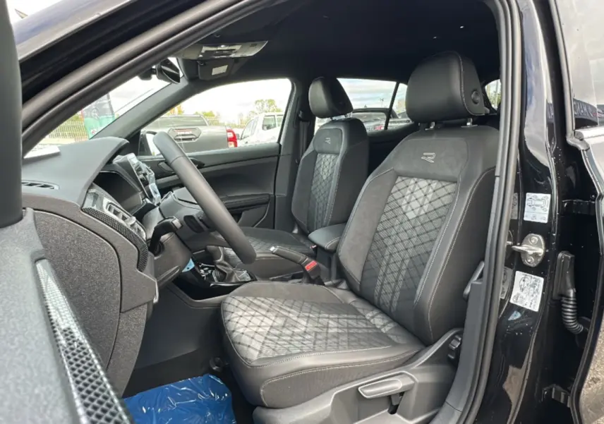 Vue intérieure côté conducteur du Volkswagen T-Cross TSI 116 DSG7 R-Line 2025 avec sièges tissu noirs et logo R brodé.