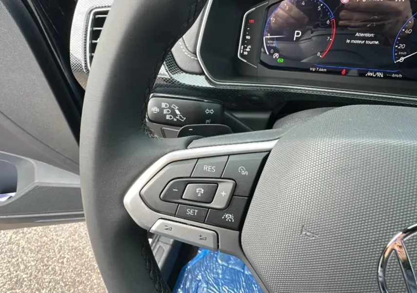 Gros plan sur le volant cuir multifonctions du Volkswagen T-Cross noir intense 2025, affichage digital en arrière-plan.