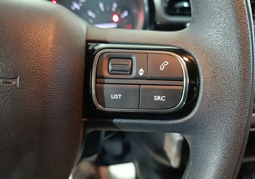 Gros plan sur les commandes gauche du volant noir du Citroën C3 2024, boutons pour appels et listes multimédias.