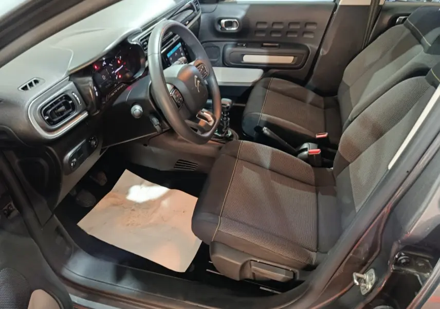 Vue intérieure côté conducteur de la Citroën C3 gris foncé 2024, montrant sièges tissu et tableau de bord moderne.