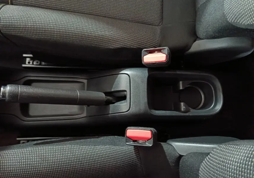 Vue plongeante sur la console centrale noire de la Citroën C3 2024, avec frein à main manuel et deux ceintures rouges.