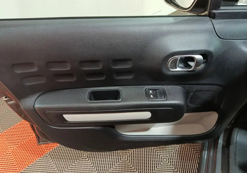 Vue intérieure côté gauche de la porte avant d'une Citroën C3 gris foncé, avec commandes de vitres et poignée argentée.