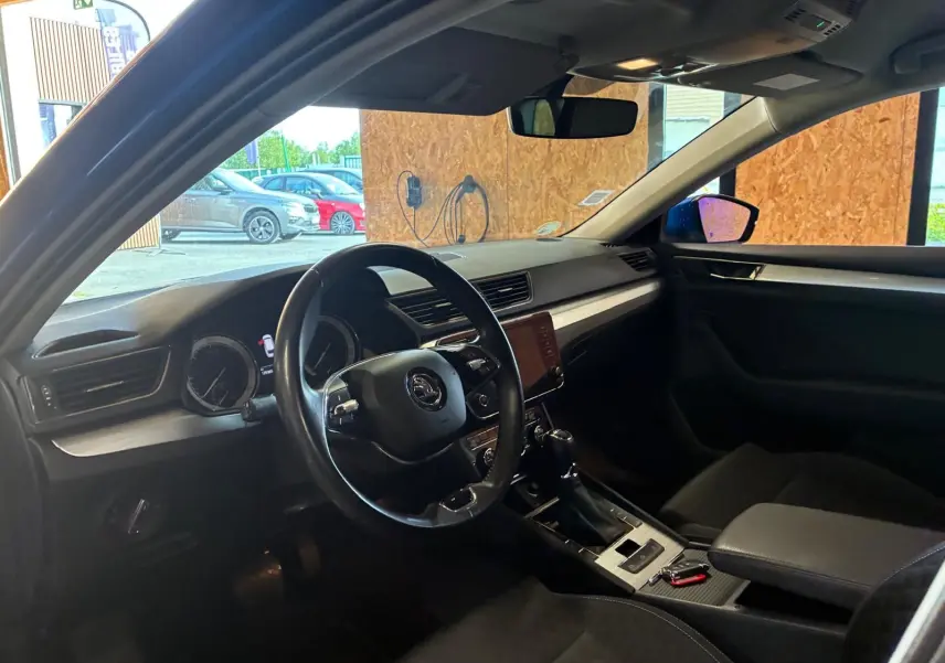 Vue intérieure côté conducteur du Skoda Superb Combi 2021, tableau de bord et volant noirs avec écran central tactile.