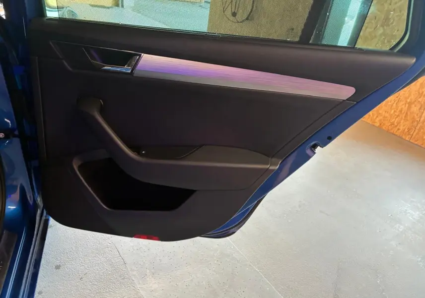 Gros plan sur la porte arrière gauche ouverte d'une Skoda Superb Combi bleu, avec garniture intérieure noire et insert argenté.
