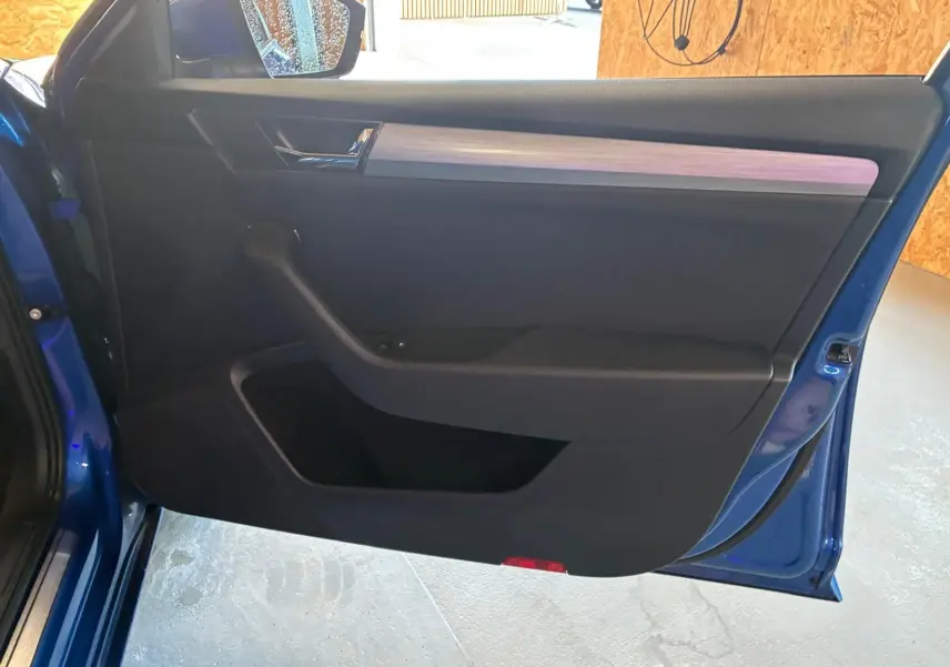 Vue intérieure de la porte avant gauche d'une Skoda Superb Combi bleu 2021 avec garniture noire et insert bois clair.