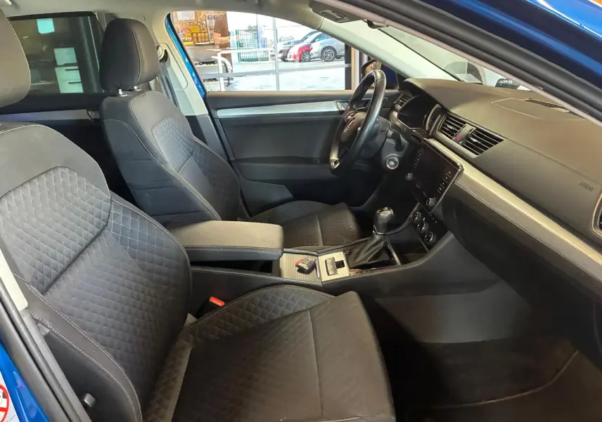 Vue intérieure côté conducteur de la Skoda Superb Combi 2021 bleu, sièges tissu noir avec console centrale et volant visibles.