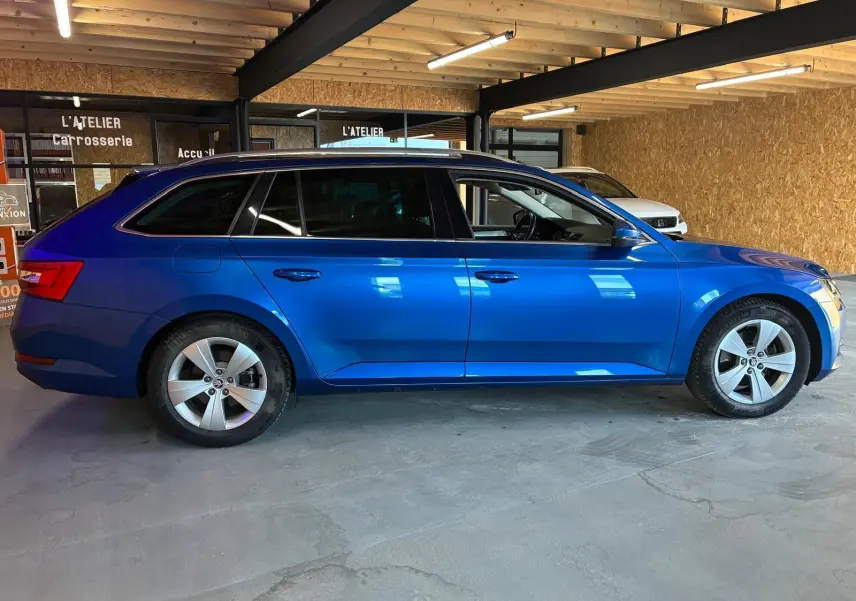 Vue latérale gauche d'une Skoda Superb Combi bleu métallisé 2021 stationnée en intérieur avec jantes alliage 5 branches.