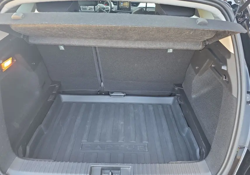 Coffre ouvert vu de l'arrière d'un Renault Captur noir, avec tapis de coffre marqué "CAPTUR" et intérieur sombre.