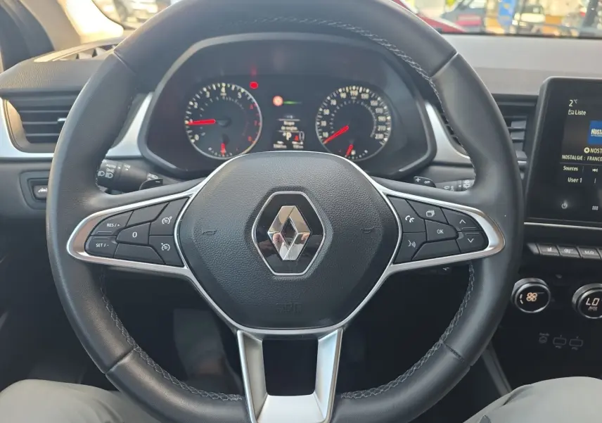 Vue centrée du volant noir de Renault Captur 2021 avec commandes intégrées et tableau de bord en arrière-plan.