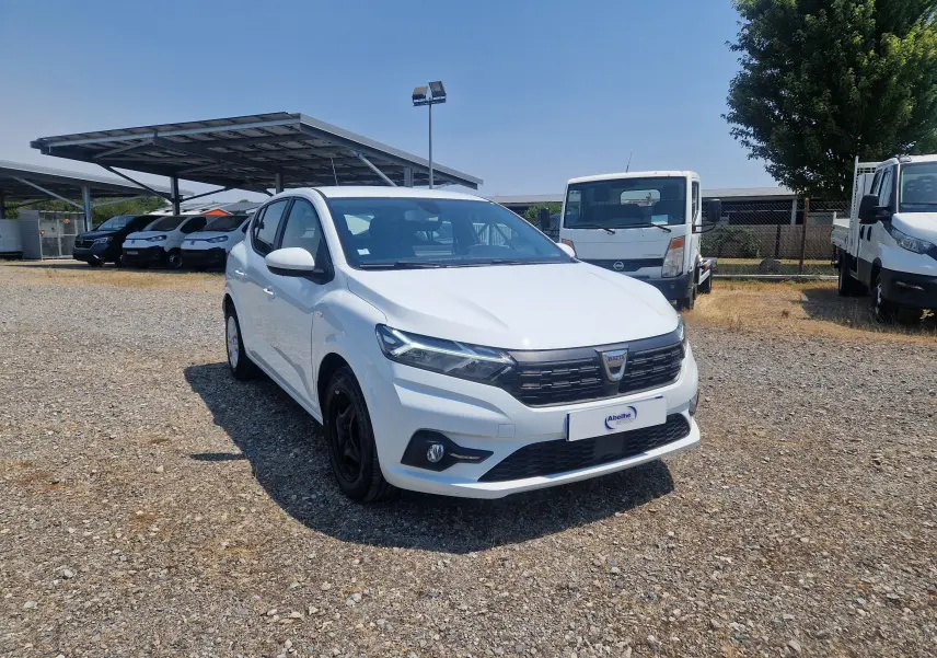 Vue 3/4 avant gauche d'une Dacia Sandero blanche 2022, avec calandre noire et feux LED distinctifs.