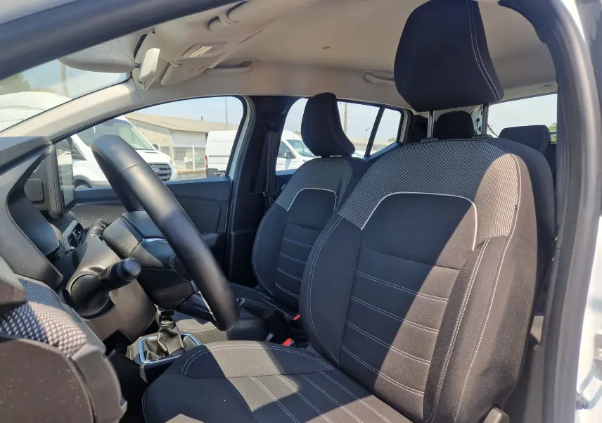 Vue intérieure côté conducteur de la Dacia Sandero blanche 2022, montrant les sièges noirs et la boîte manuelle.