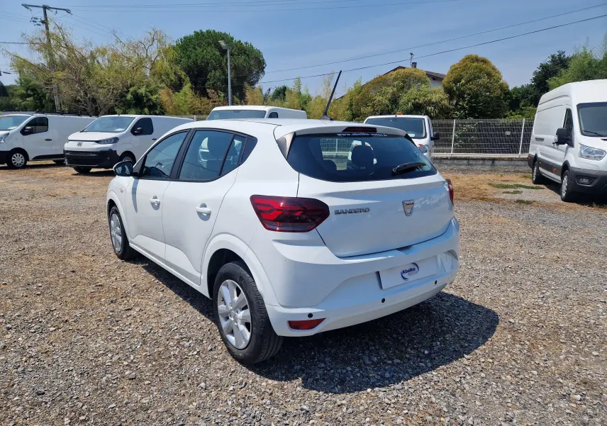Vue 3/4 arrière droite d'une Dacia Sandero blanche 2022, version Confort, sur un parking extérieur ensoleillé.
