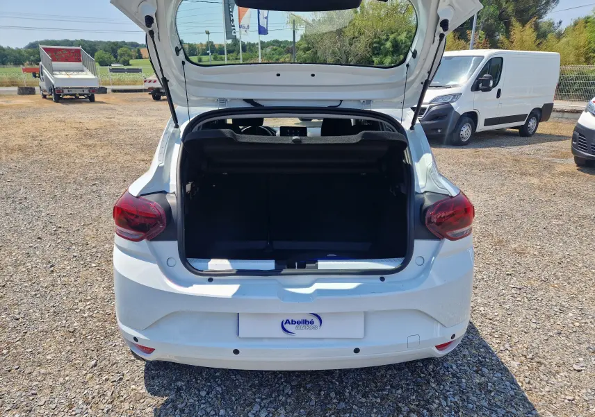 Vue arrière d'une Dacia Sandero blanche 2022 avec coffre ouvert sur un parking ensoleillé.