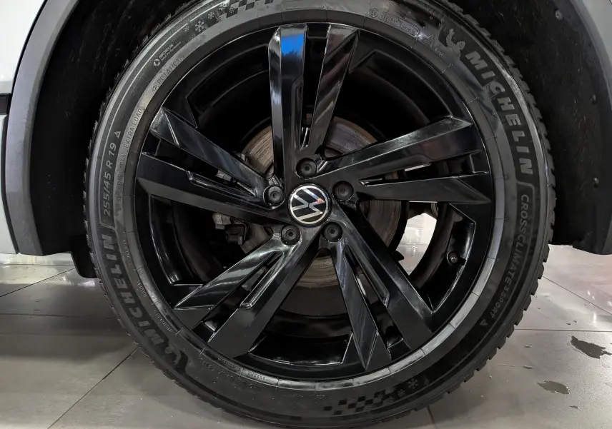 Gros plan sur la jante noire brillante de 19 pouces avec logo Volkswagen, montée sur un Volkswagen Tiguan reflet d'argent.