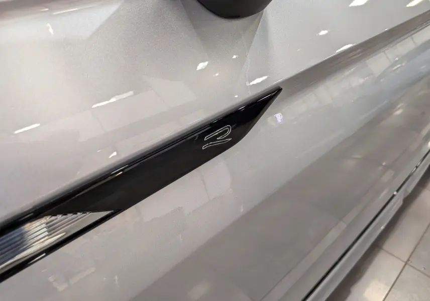 Gros plan sur la prise d'air latérale noire avec logo R du Volkswagen Tiguan 2024 en reflet d'argent, côté gauche.