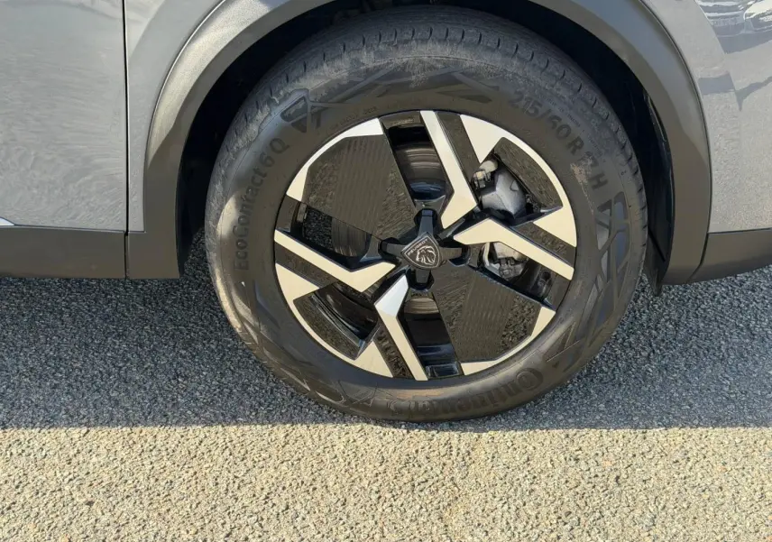 Gros plan sur la roue avant droite avec jante alu bicolore du Peugeot e-2008 gris Artense.