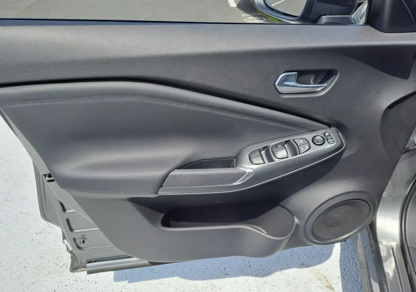 Porte côté gauche ouverte du Nissan Juke Hybrid 143 N-Connecta gris squale, avec commandes de vitres et haut-parleur intégré visible.