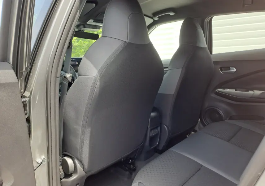 Vue intérieure arrière côté gauche du Nissan Juke Hybrid gris squale, montrant les sièges avant et banquette arrière en tissu noir.