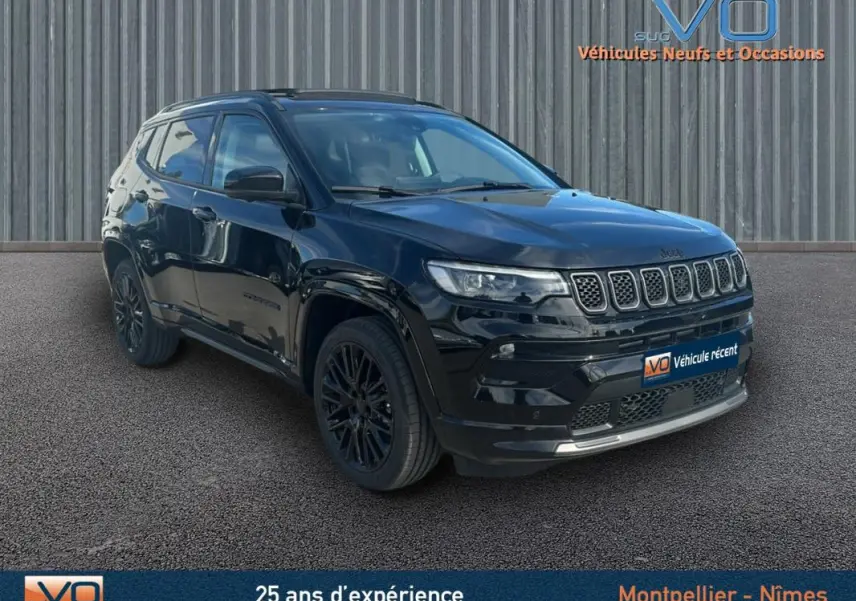 Jeep Compass noir en 3/4 avant droit, avec barres de toit et jantes alliage noires, stationné devant un mur métallique.