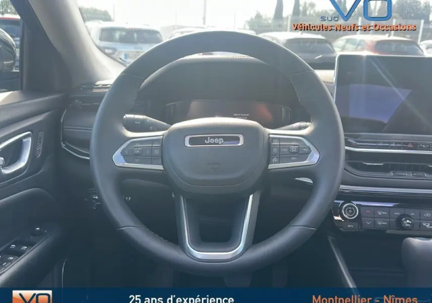 Vue centrée sur le volant cuir du Jeep Compass 2023 avec tableau de bord et écran tactile en arrière-plan.