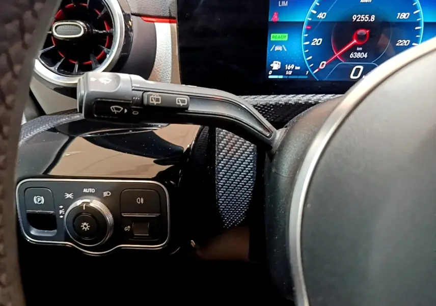 Vue rapprochée du volant cuir et du tableau de bord numérique bleu de la Mercedes Classe A blanche, avec commandes éclairage.