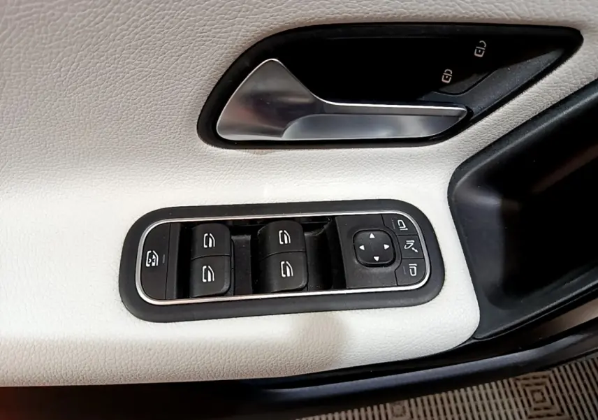 Gros plan sur la commande des vitres et la poignée de porte côté conducteur en cuir blanc de la Mercedes Classe A Berline.