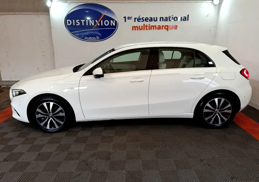 Profil côté gauche d'une Mercedes Classe A Berline blanche, vue en intérieur avec jantes alliage et feux arrière allumés.